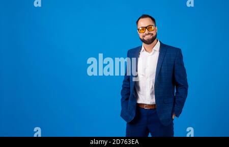Jeune homme portant des lunettes de soleil dans un costume bleu classique un arrière-plan bleu Banque D'Images