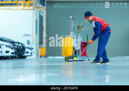 Un travailleur asiatique dans un centre de réparation de mécanicien de voiture nettoie à l'aide de balais pour rouler l'eau du sol en époxy. Balais dans le centre de réparation de voiture. Banque D'Images