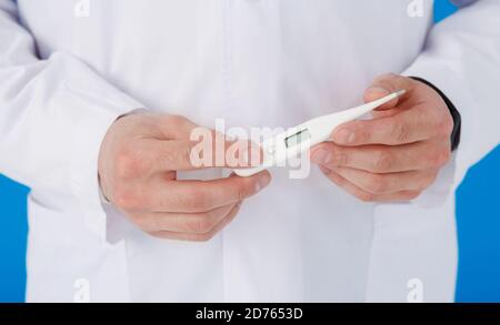 Gros plan du thermomètre en caoutchouc bleu gant main habillée, homme poitrine en robe médicale blanche sur un fond flou Banque D'Images