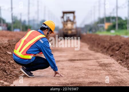 L'ingénieur civil vérifie la surface du sol et contrôle le sol jaune vibrant et la niveleuse compacteur civil travaillant sur le chantier de construction de routes. Banque D'Images
