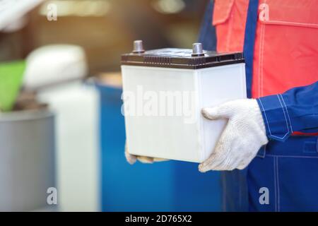 Gros technicien ou mécanicien de bord tenant la batterie de la voiture dans le centre de réparation automobile. Banque D'Images