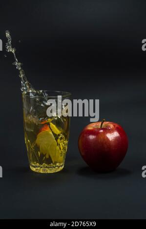 Tranche de pomme projetée dans le verre éclaboussant le jus de pomme. Belle pomme rouge à côté. Banque D'Images