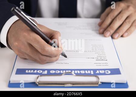 L'agent d'assurance Zoom écrit à la main le formulaire de demande de remboursement d'assurance automobile ou Document d'assurance sur la table de bureau Banque D'Images