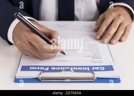 L'agent d'assurance rédige à la main un formulaire de demande de remboursement d'assurance automobile ou une assurance Document sur la table Office Banque D'Images