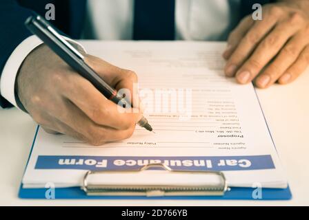 L'agent d'assurance Zoom écrit à la main le formulaire de demande de remboursement d'assurance automobile ou Document d'assurance sur la table de bureau en tons anciens Banque D'Images