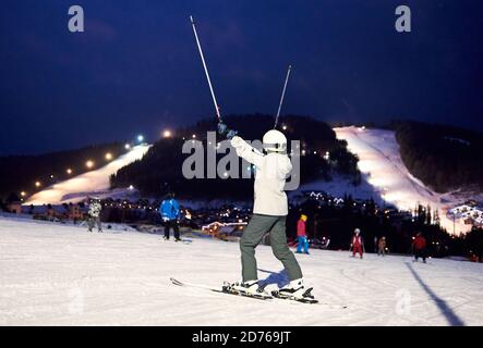 Vue arrière du skieur femelle se réjouissant de lever les mains avec des bâtons de ski. Fin heureuse de la journée d'hiver de ski sportif actif à la station de ski. Sur le moun d'arrière-plan Banque D'Images