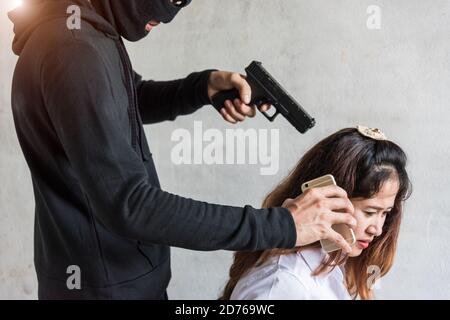 Criminel ou terroriste en noir tenant une arme à la jeune femme pour appeler de l'argent otage, le concept de voleur Banque D'Images
