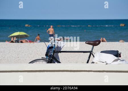 Un vélo à gauche, adoché à un mur sur le front de mer de Marotta, sous la lumière du soleil de l'été. Quelques touristes et la mer adriatique sur le fond Banque D'Images