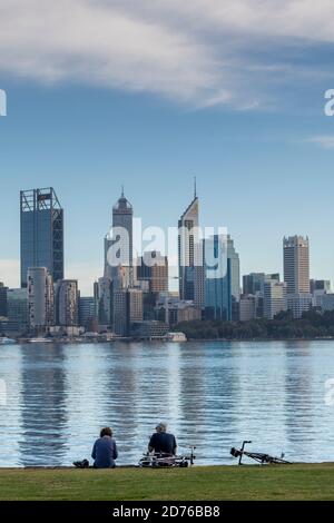 Couple assis sur les rives de la Swan River en face du quartier des affaires de Perth. Banque D'Images