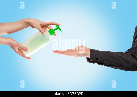 Une femme dépose du savon liquide sur la paume de l'homme pour la désinfection. Gros plan des mains sur fond bleu. Copier l'espace. Le concept de désinfection et virus p Banque D'Images