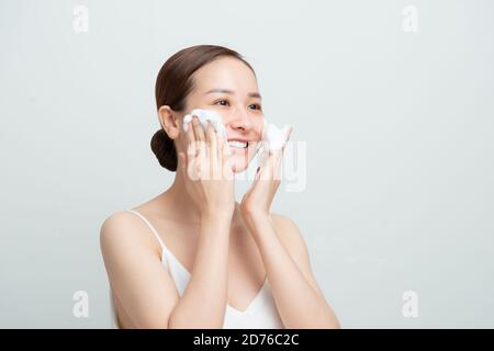 Sourire belle fille asiatique en utilisant le nettoyant moussant. Concept de lavage du visage isolé sur fond blanc. Banque D'Images