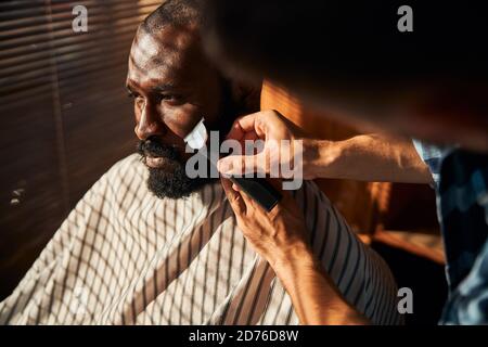 Barbe rasage de la barbe du client avec tondeuse électrique dans un salon de coiffure Banque D'Images