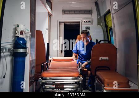 Jeune médecin en uniforme médical assis dans la voiture d'ambulance. Banque D'Images