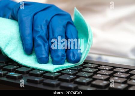 La main de la fille dans un gant de protection bleu nettoie le clavier avec un chiffon pour la prévention des coronavirus, des bactéries, des virus et des germes. Banque D'Images