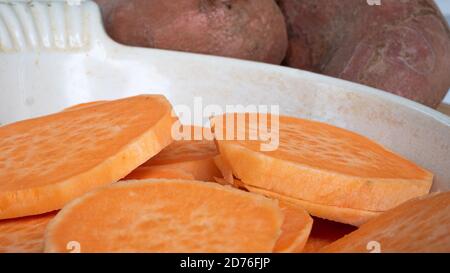 Tranchez les patates douces l'une sur l'autre dans une casserole en céramique. L'agrafe orange vif est un substitut sain pour la pomme de terre ou les frites. Banque D'Images