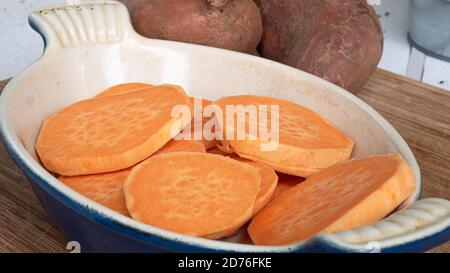 Tranchez les patates douces l'une sur l'autre dans une casserole en céramique. L'agrafe orange vif est un substitut sain pour la pomme de terre ou les frites. Banque D'Images