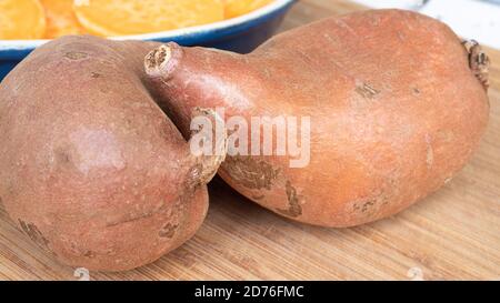 Deux patates douces en vedette, placées sur une planche de bois. L'agrafe orange vif est un substitut sain pour la pomme de terre ou les frites. Banque D'Images