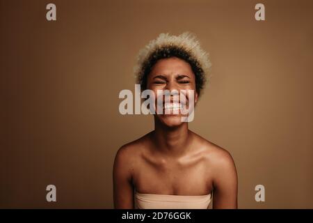 Femme afro-américaine riant avec les yeux fermés. Gros plan sur une femme afro-américaine sur fond marron. Banque D'Images