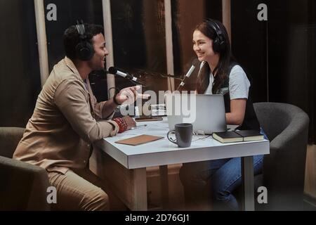 Portait de deux heureux hôtes de radio, jeune homme et femme souriant tout en discutant de divers sujets, modérant un spectacle en studio Banque D'Images