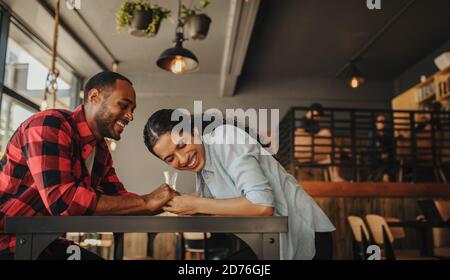 Homme et femme souriants assis dans un café tenant la main. Couple amoureux assis dans un café souriant et ayant un grand séjour ensemble. Banque D'Images