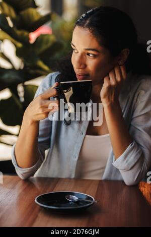 Femme africaine assise au café prenant un café. Femme prenant un café au café-restaurant et regardant loin. Banque D'Images