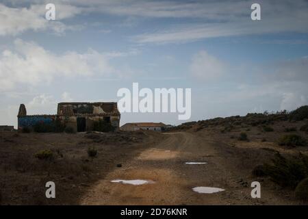 Vieille route de terre avec des trous de flaque d'eau sur le sol, en passant par une maison abandonnée en ruines. Jour nuageux Banque D'Images