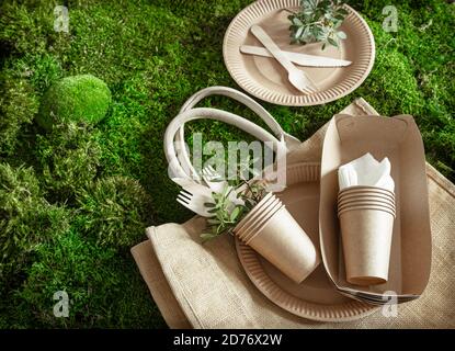 Vaisselle écologique, jetable et recyclable. Boîtes à nourriture en papier, assiettes et couverts de fécule de maïs sur fond d'herbe verte . Banque D'Images