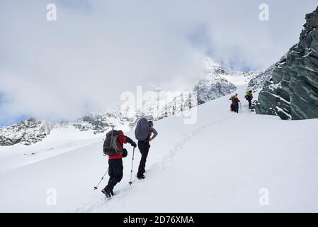 Les hommes voyageant avec des sacs à dos marchent en montant dans les montagnes d'hiver. Groupe d'alpinistes avec des bâtons de randonnée marchant dans la neige et se dirigeant vers la montagne Banque D'Images