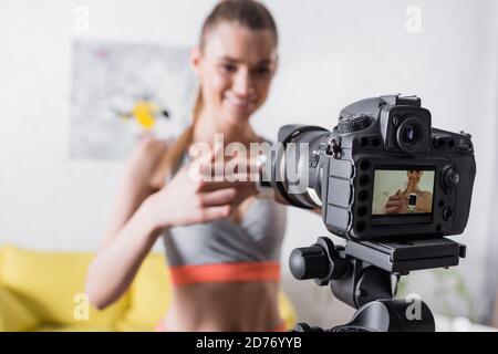 Mise au point sélective d'une sportswoman souriante pointant vers une montre intelligente proche du numérique appareil photo Banque D'Images