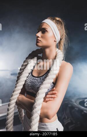 Jeune sportif avec bras croisés et corde de combat debout salle de sport avec fumée Banque D'Images