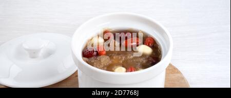 Gros plan de la soupe traditionnelle chinoise douce aux champignons blancs avec graines de lotus, dattes rouges (jujujube) et baies de carcajou (goji, gogyberry) sur fond blanc. Banque D'Images