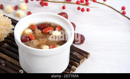 Gros plan de la soupe traditionnelle chinoise douce aux champignons blancs avec graines de lotus, dattes rouges (jujujube) et baies de carcajou (goji, gogyberry) sur fond blanc. Banque D'Images