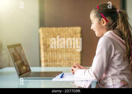 Jolie fille d'école élégante étudiant les mathématiques de devoirs pendant sa leçon en ligne à la maison. Enseignant sur l'écran de l'ordinateur Banque D'Images