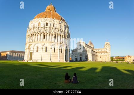 Les touristes s'assoient sur l'herbe en face du Baptistère de San Giovanni à Pise, Toscane, Italie Banque D'Images