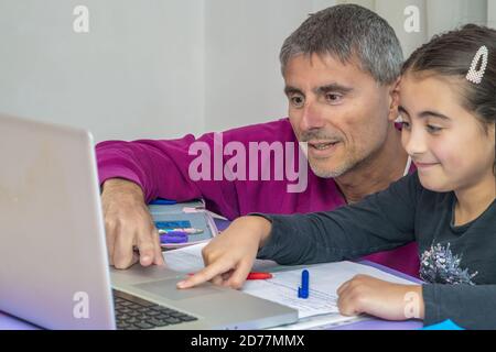 Jeune écolière étudiant les devoirs pendant sa leçon en ligne à la maison avec son père, distance sociale pendant la quarantaine, auto-isolement, educati en ligne Banque D'Images