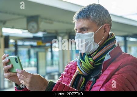 Homme avec un masque de santé utilisant un smartphone à la gare vide en cas de pandémie de covid. Banque D'Images