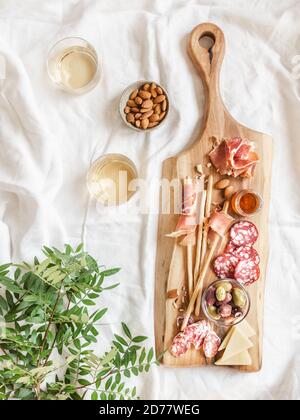 Ensemble de vins d'encas. Variété de saucisses, olives, fromage, bâtonnets de pain, sur planche à découper en bois et deux verres à vin sur une nappe blanche. Pose à plat. Haut vi Banque D'Images