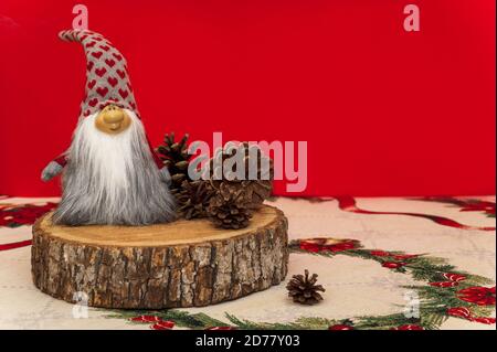 Nain de Noël placé sur une souche avec des cônes sur un arrière-plan rouge Banque D'Images