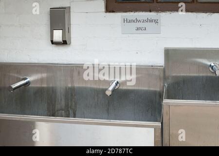 gros plan sur les installations de lavage des mains, l'évier en acier inoxydable et les robinets d'eau avec un distributeur de savon en acier inoxydable. Un mur de briques blanches à l'arrière Banque D'Images