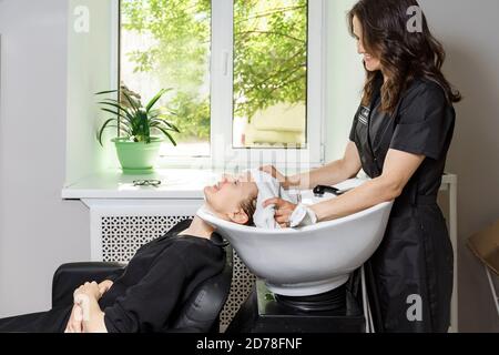 coiffeur couvre les cheveux du client avec une serviette. la jeune femme se lave les cheveux dans un salon de beauté Banque D'Images