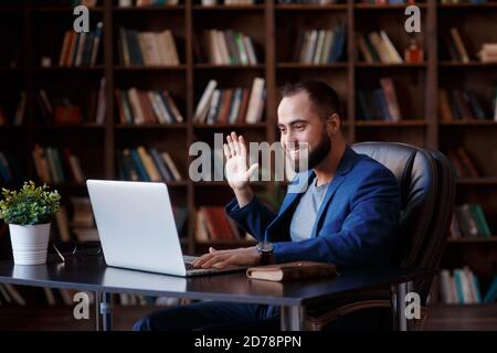 Un jeune homme d'affaires travaille sur un ordinateur portable dans un bureau luxueux de la bibliothèque. Un homme barbu, gai dans un costume bleu à un bureau est de taper sur un clavier Banque D'Images