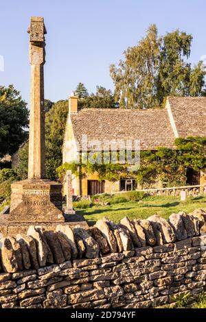 Lumière du soir sur le mémorial de guerre dans le chantier naval de St Barnabas et un cottage traditionnel en pierre dans le village de Snowshill dans les Cotswolds, Gloucestershire au Royaume-Uni Banque D'Images