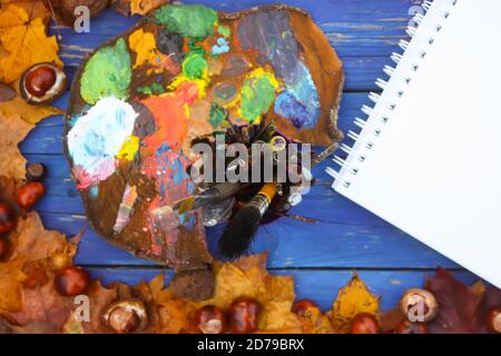 Lieu de travail de peintre dans le parc d'automne avec palette, paintpad et pinceaux. Feuilles d'automne et châtaignes sur fond de bois bleu. Banque D'Images