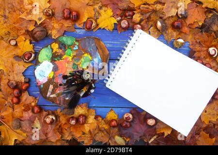 Lieu de travail pour le peintre dans le parc d'automne avec palette, paintpad et pinceaux. Feuilles d'automne et châtaignes sur fond de bois bleu. Banque D'Images