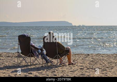 L'homme et la femme se sont enveloppés contre le froid en profitant du soleil Sur Avon Beach UK avec Isle of Wight Needles in La distance Banque D'Images