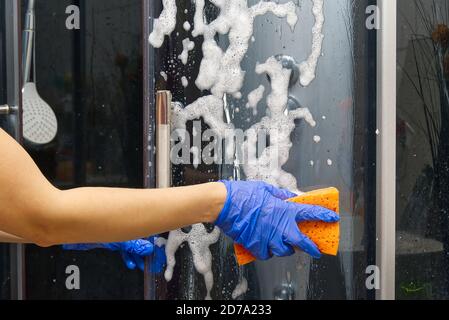 Nettoyage des cabines de vapeur de douche des dépôts de calcium. Nettoyage dans la salle de bains. Mains dans les gants avec un chiffon et détergent lave la douche et le verre Banque D'Images