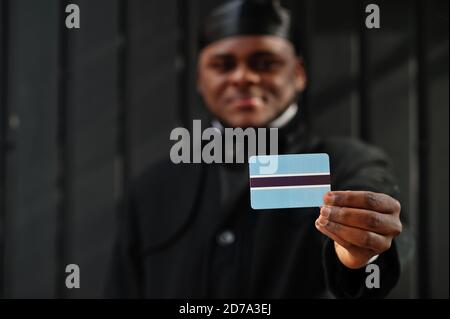 L'homme africain porte du durag noir tient le drapeau du Botswana à la main isolé arrière-plan sombre. Banque D'Images