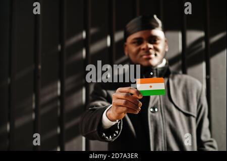 L'homme africain porte du durag noir tient le drapeau du Niger à la main isolé arrière-plan sombre. Banque D'Images