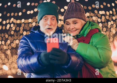 Génial. Photo de deux personnes retraités amis couple tenir téléphone recevoir email santa promesse présente port manteau rouge foulard port de tête x-mas rue soir Banque D'Images
