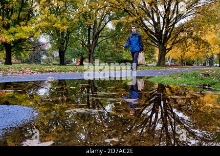 Homme qui revient de la marche dans le parc de la ville d'automne avec réflexion dans la grande flaque d'eau. Banque D'Images